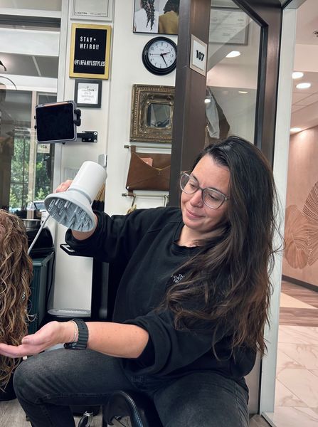 A woman with long brown hair is sitting in front of a wooden wall.