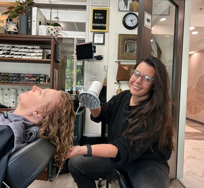 A woman with long gray hair is standing in front of a sign that says salon 33.