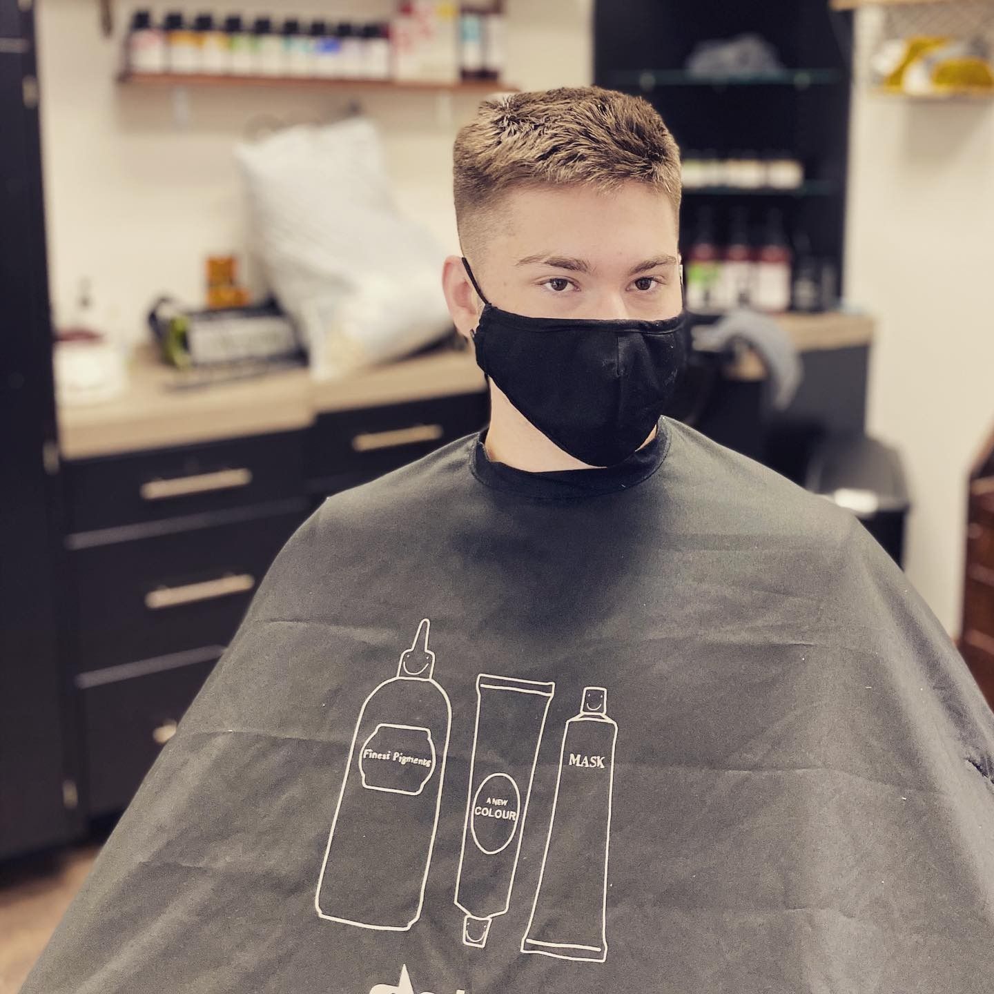 A man wearing a black face mask is getting his hair cut