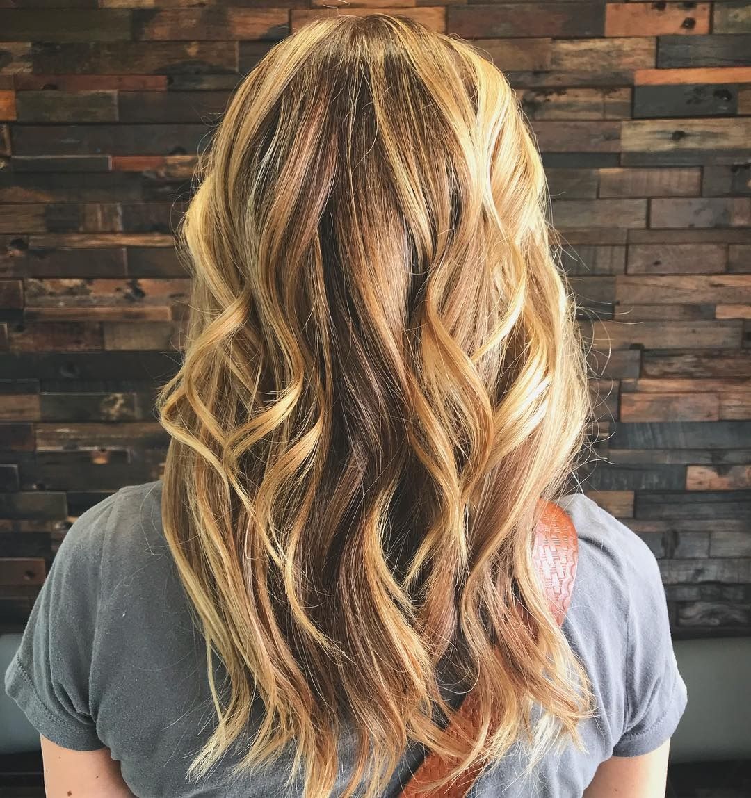 A woman with long blonde hair is standing in front of a wooden wall.