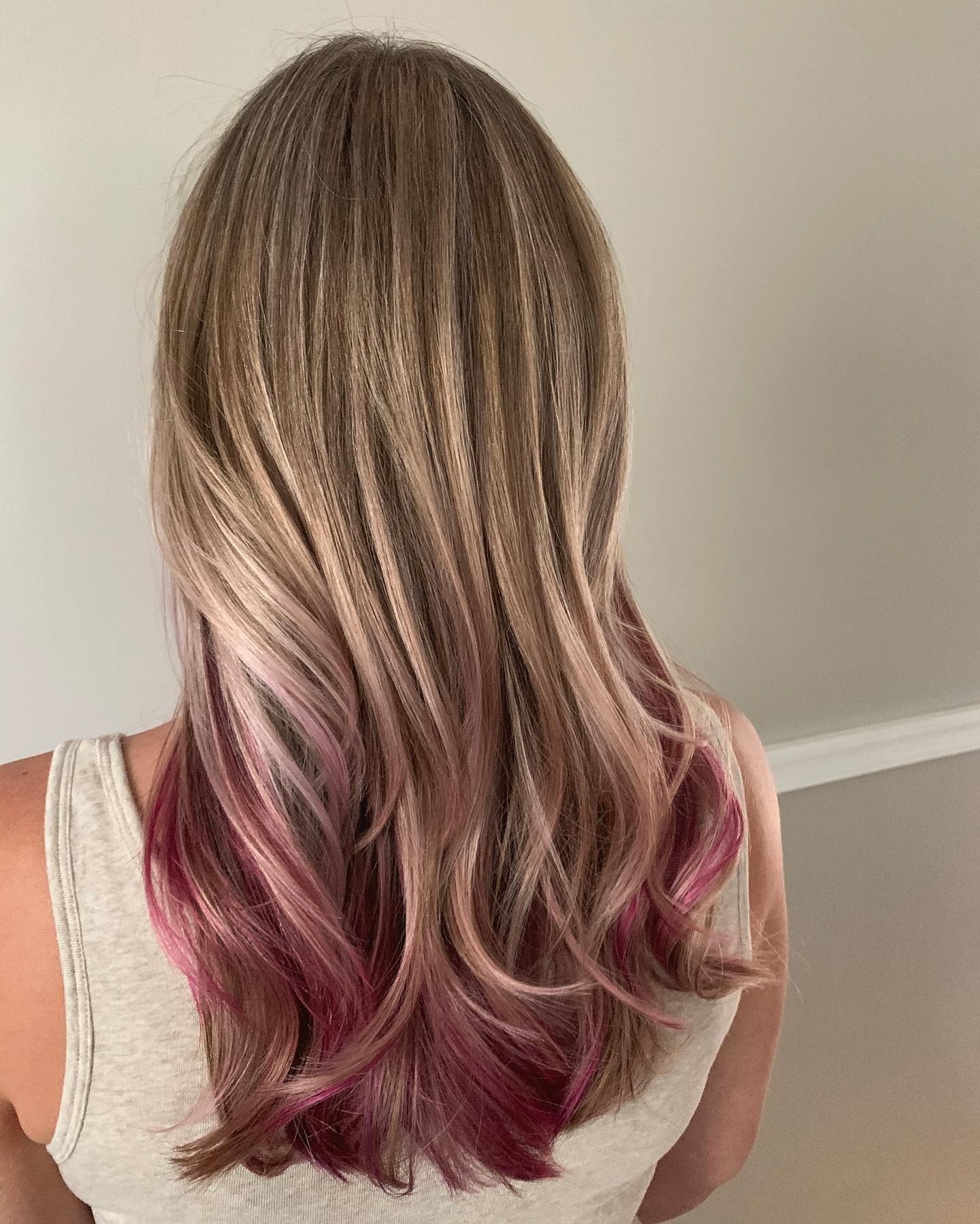 A woman with blonde hair and pink highlights is wearing a white tank top.
