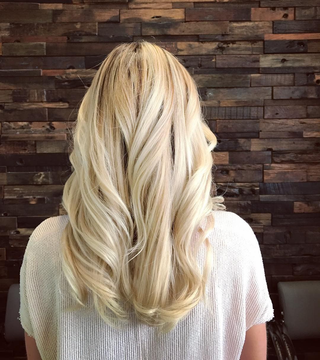 A woman with long blonde hair is standing in front of a wooden wall.