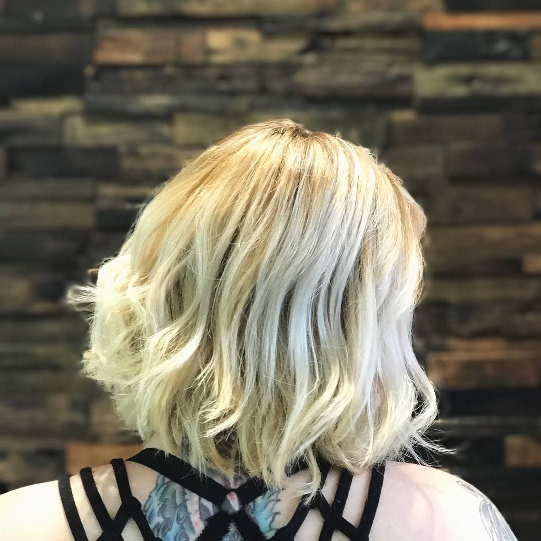 A woman with blonde hair and a tattoo on her back is standing in front of a wooden wall.