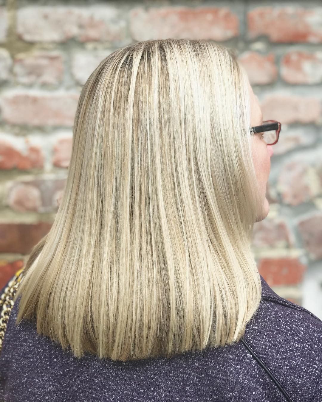A woman with blonde hair and glasses is standing in front of a brick wall.