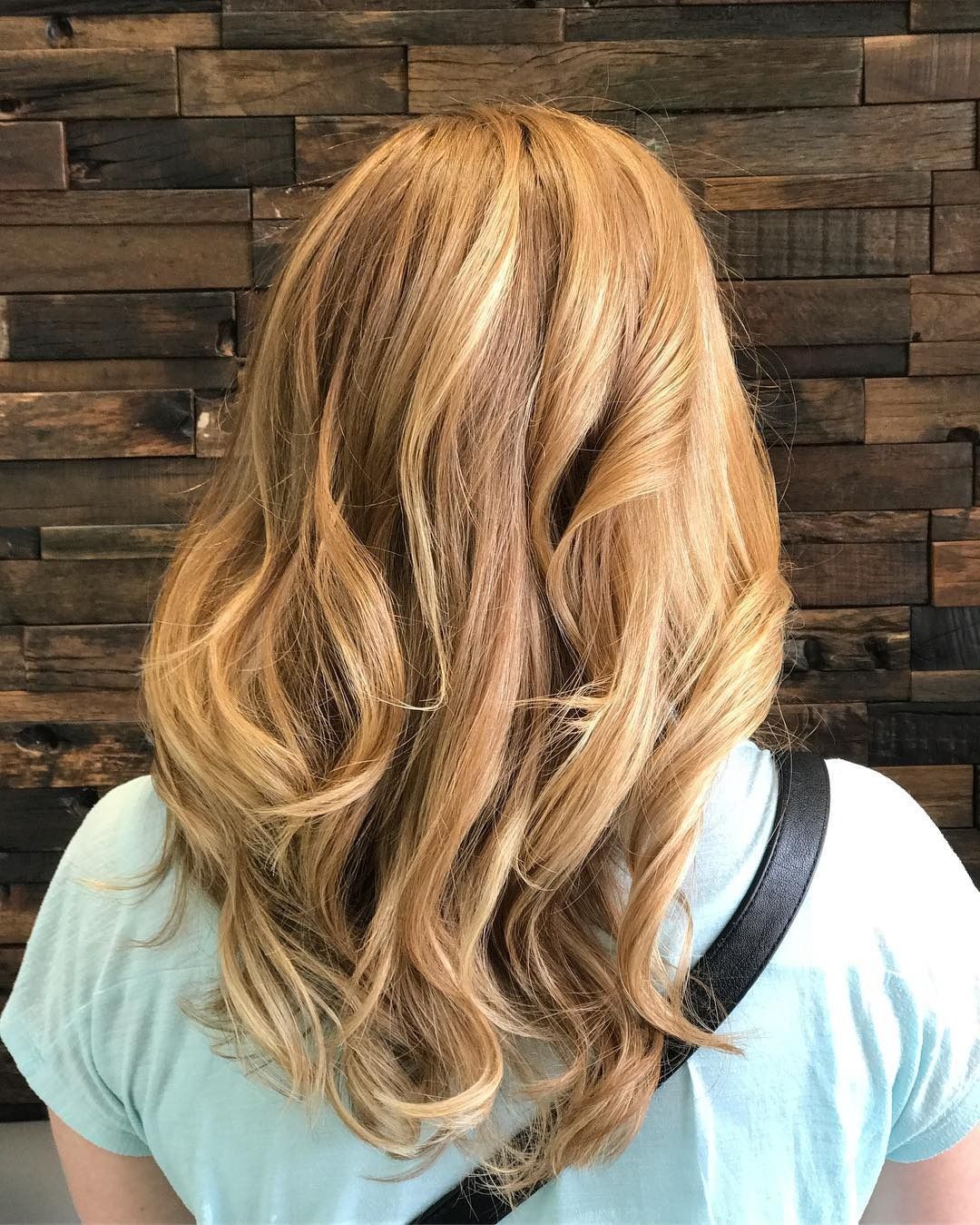 A woman with long blonde hair is standing in front of a wooden wall.