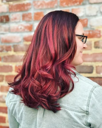A woman with red hair and glasses is standing in front of a brick wall.