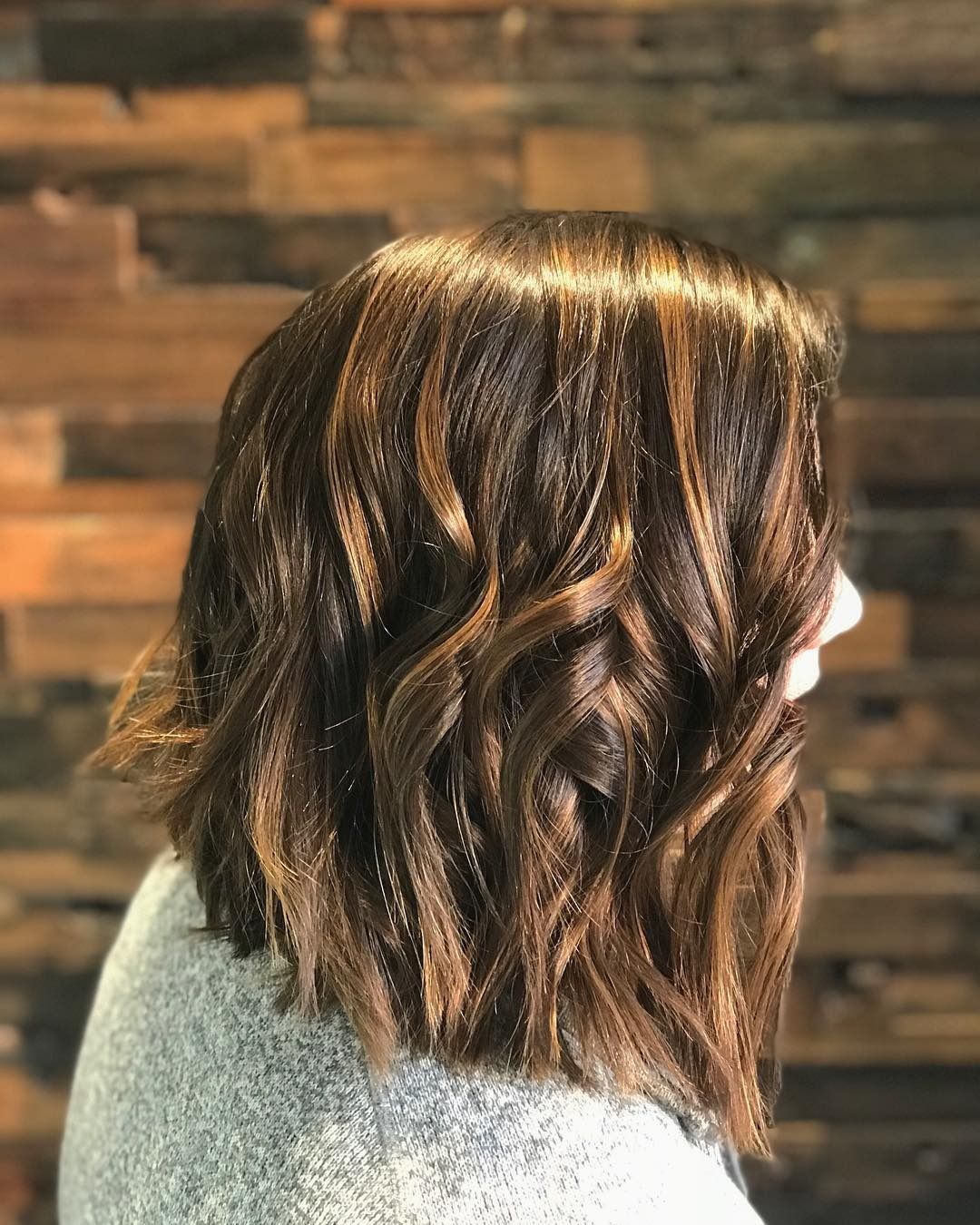 A woman with short brown hair is standing in front of a wooden wall.