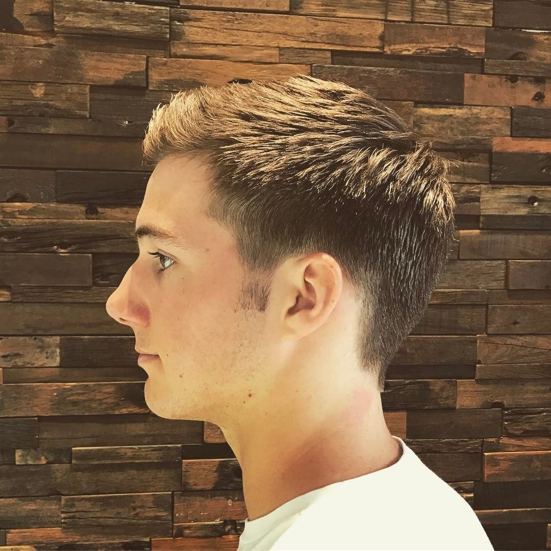 A young man with short hair is standing in front of a wooden wall.