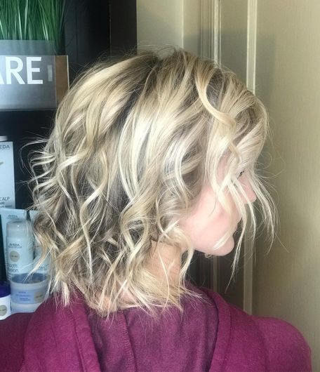 A woman with blonde curly hair is wearing a purple sweater.