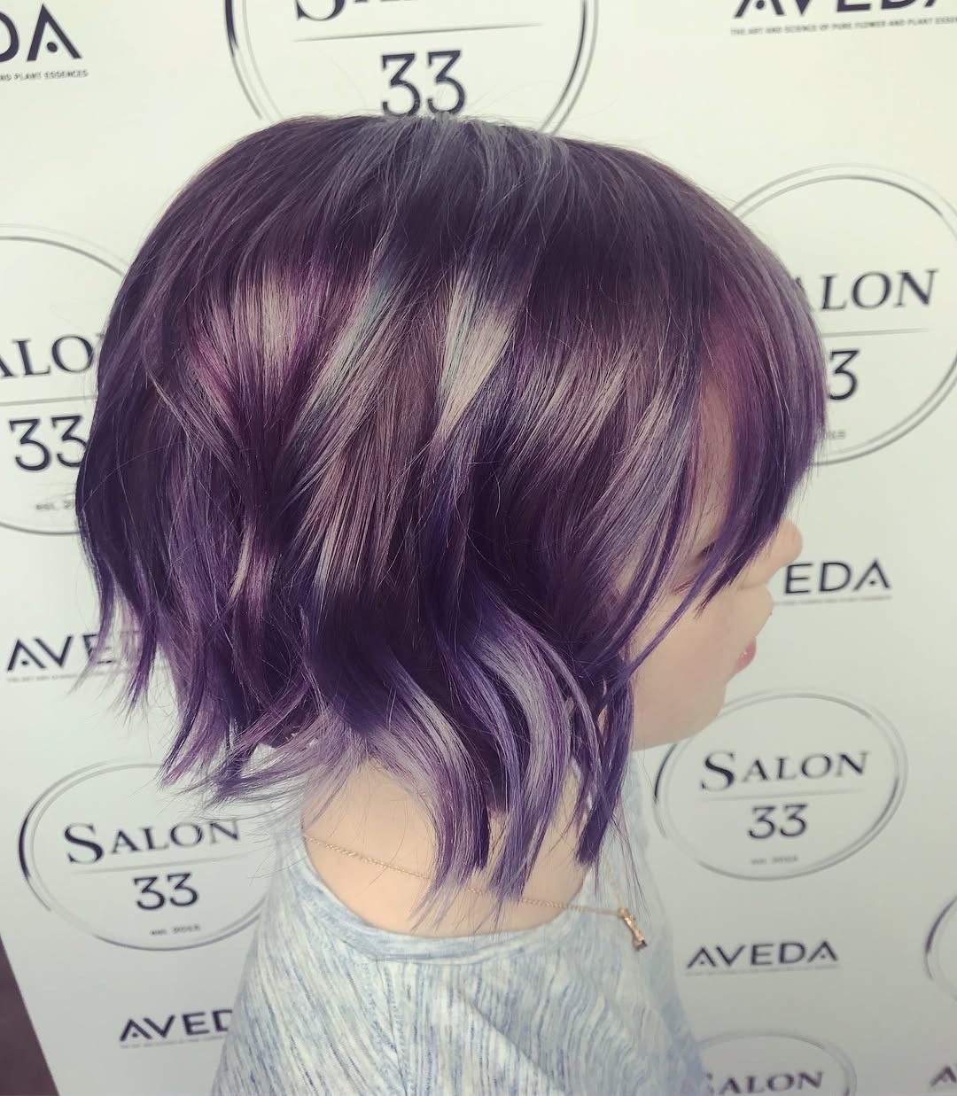 A woman with purple hair is standing in front of a sign that says salon 33