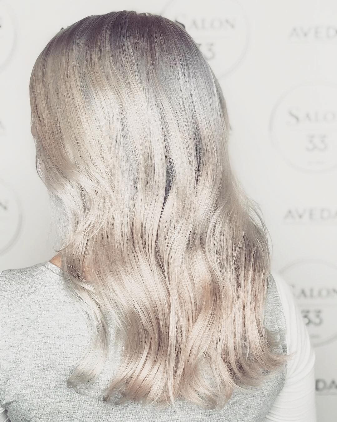 A woman with long blonde hair is wearing a grey sweater.