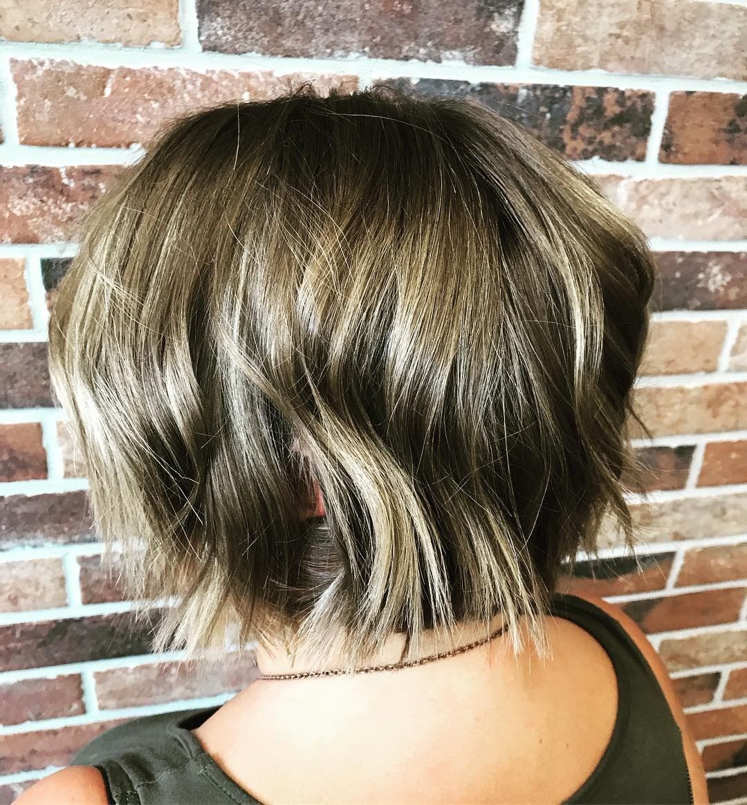 A woman with short hair is standing in front of a brick wall