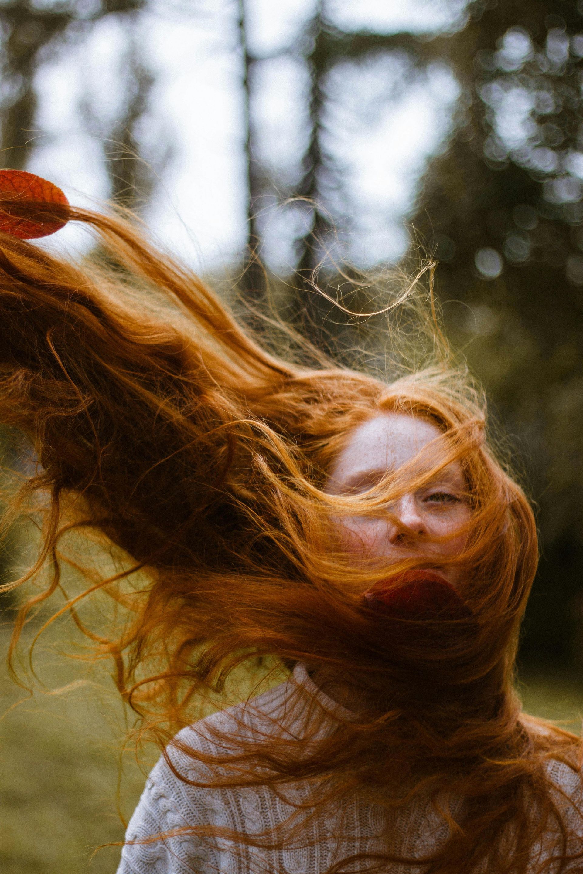 Woman with long red hair blowing in the wind outdoors, obscuring her face.