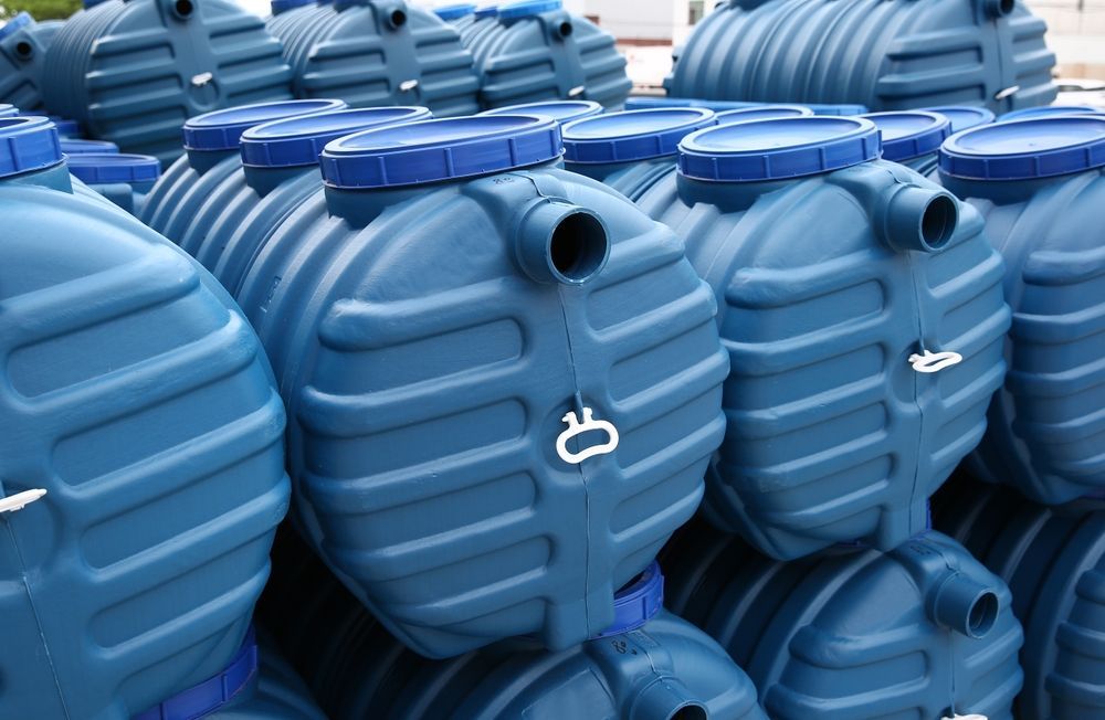 Rows of blue plastic water tanks with lids and side openings, stacked outdoors
