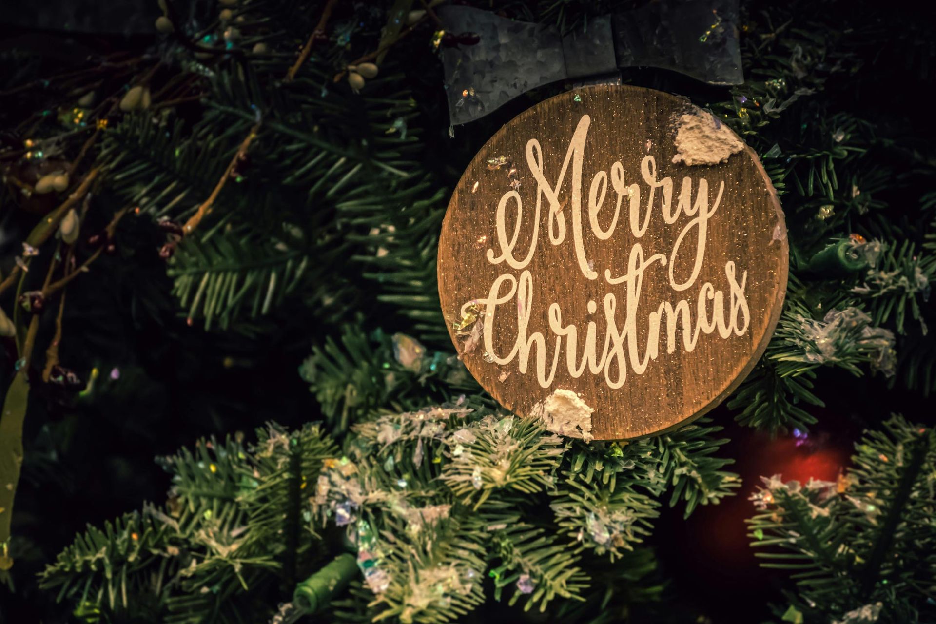 A merry christmas ornament is hanging on a christmas tree.