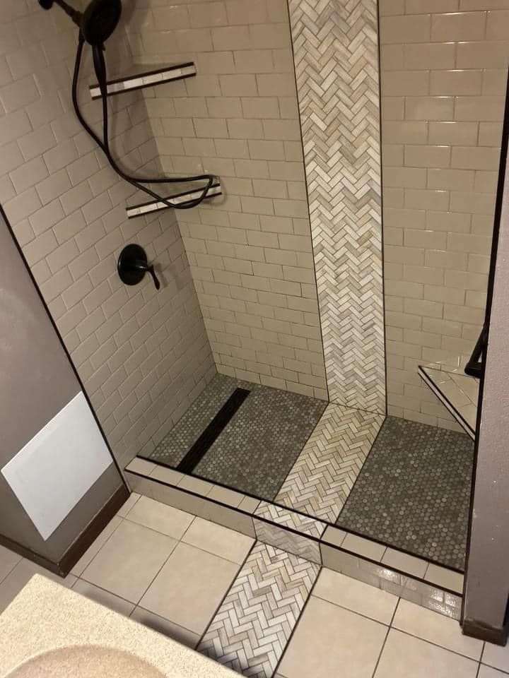 Shower with gray brick-like tiles, a herringbone accent, dark fixtures, and a curbless entry with a linear drain.