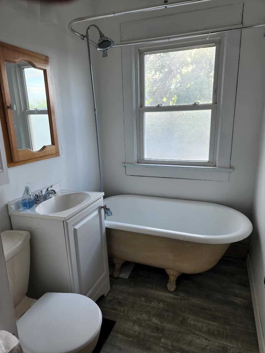 Small bathroom with a clawfoot tub, sink, toilet, window, and mirror.