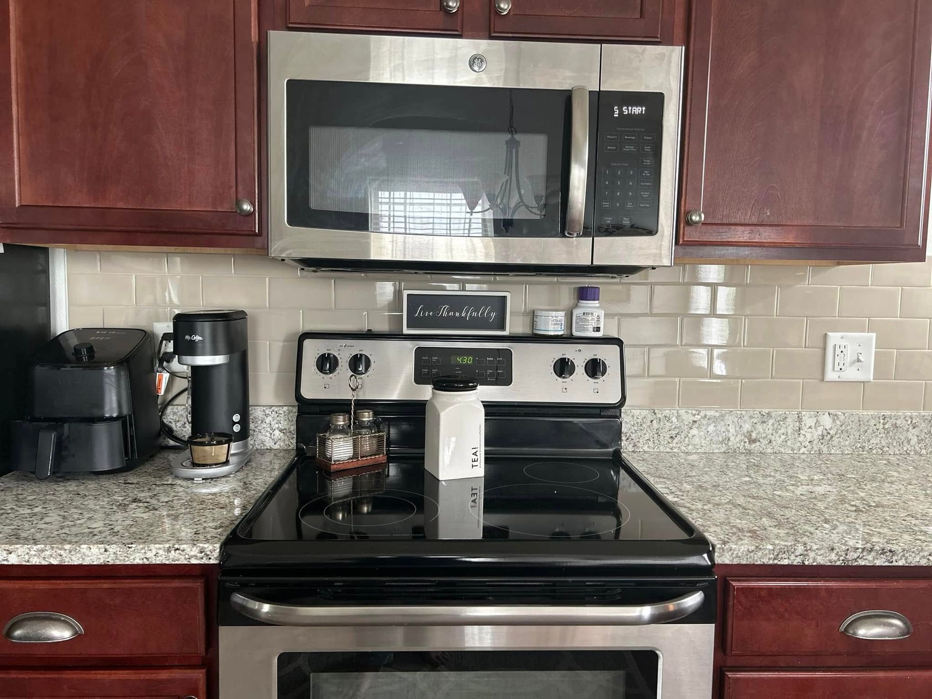 Kitchen with stainless steel appliances, dark cabinets, granite countertop, and tile backsplash.