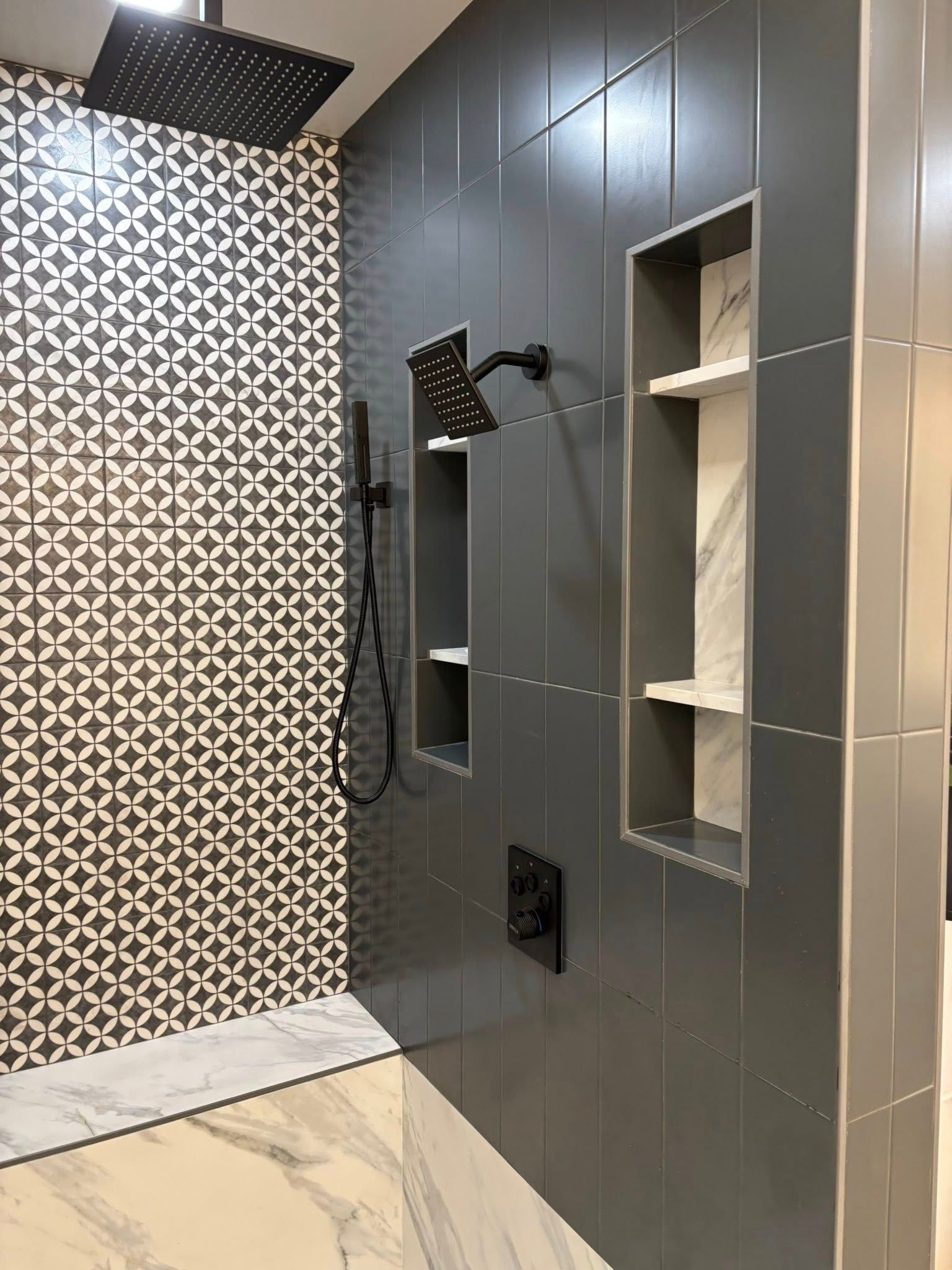 Bathroom shower with patterned tile wall, gray accent wall with built-in shelves, marble floor.