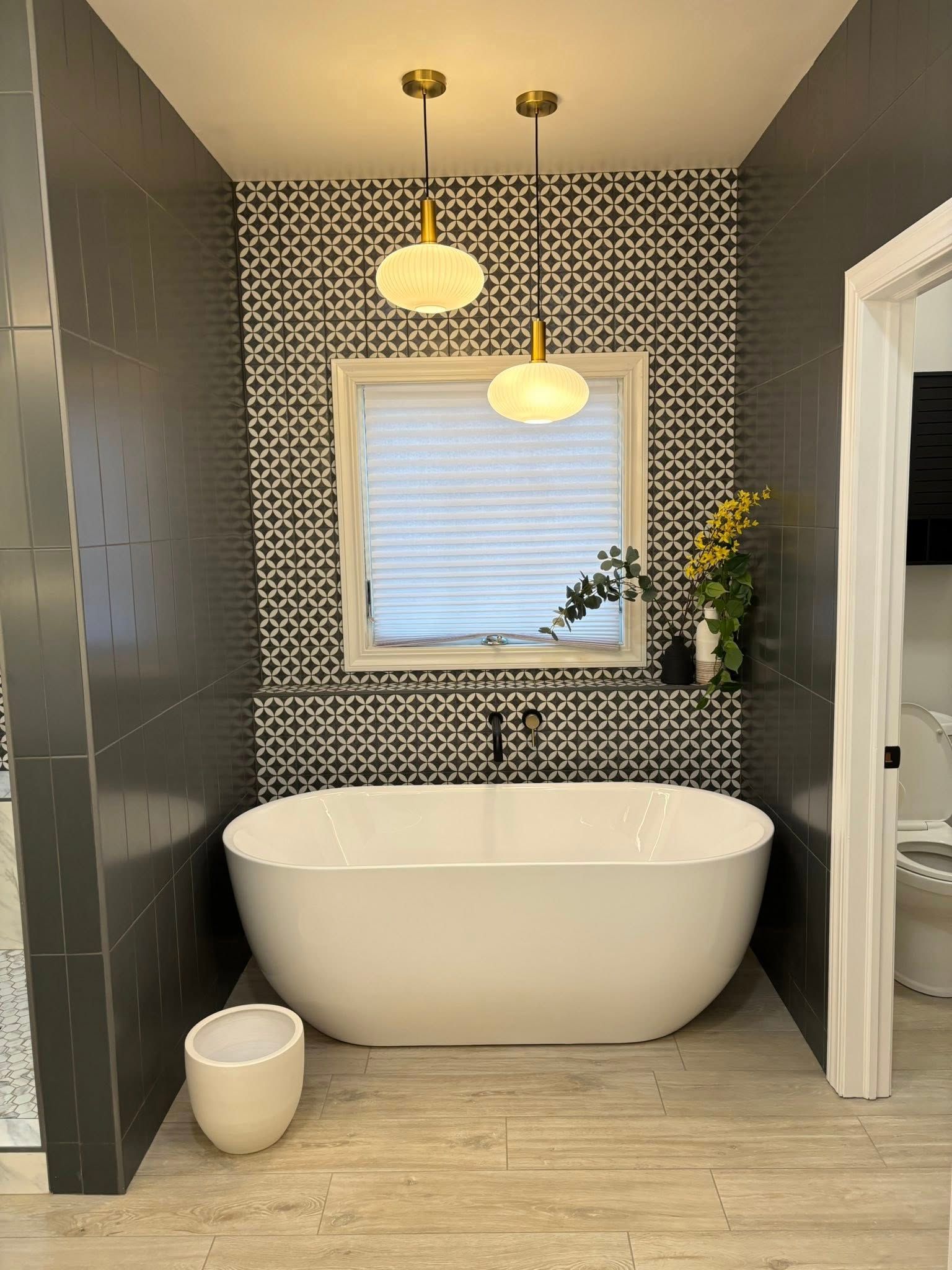 Bathroom with white tub, patterned tile wall, window, and pendant lights.
