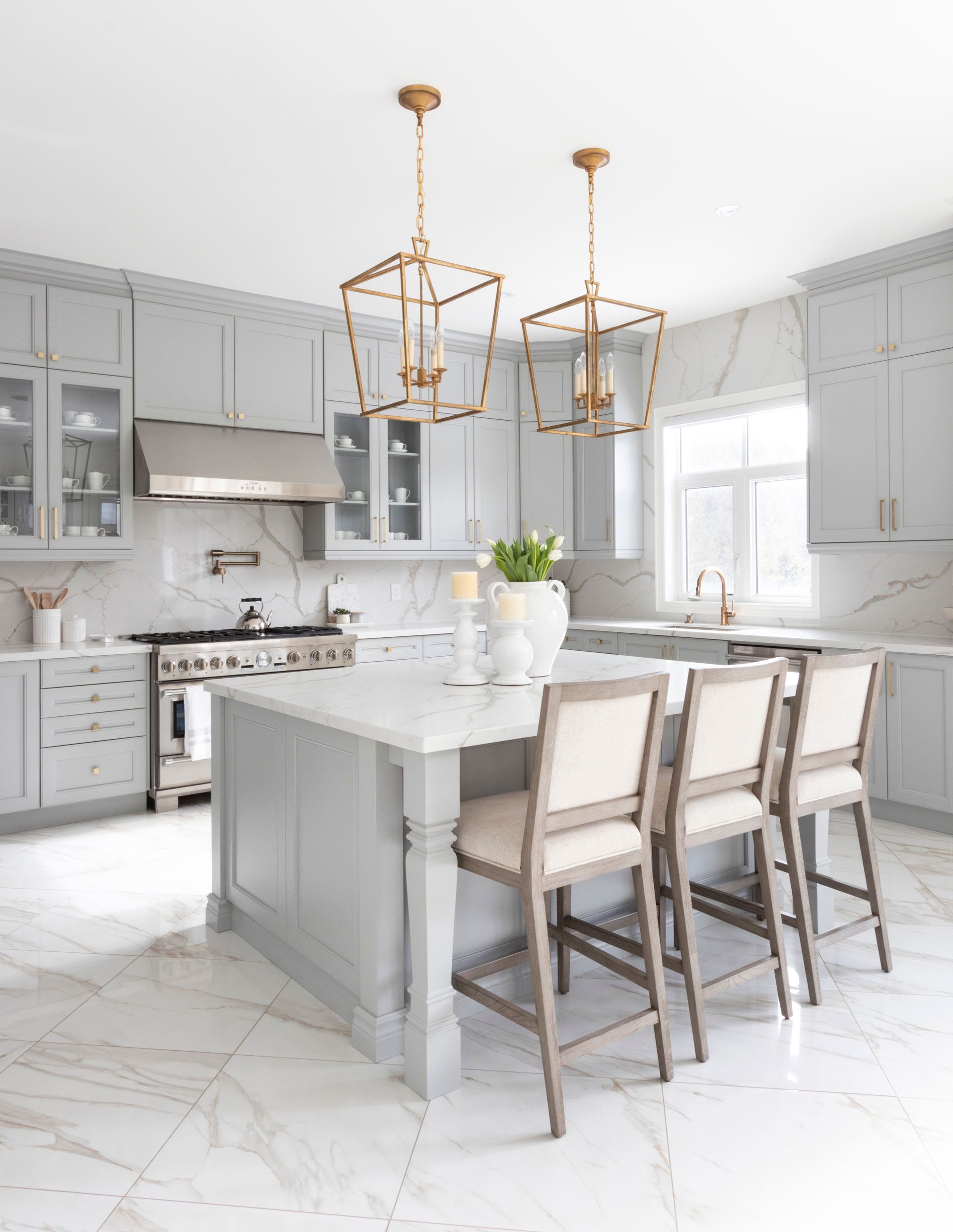 Elegant gray and white kitchen with island, pendant lights, marble countertops, and stools.