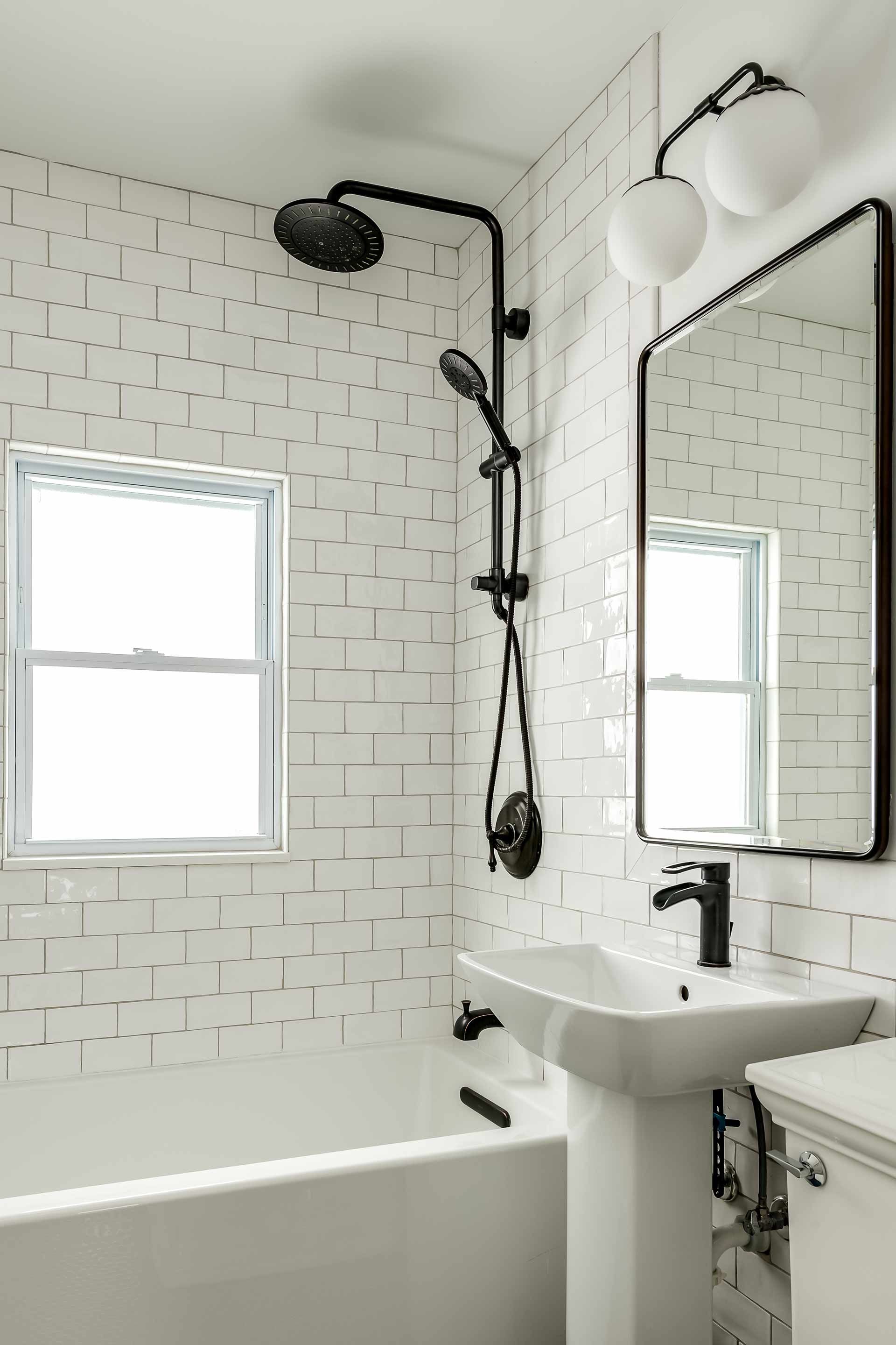 Modern white bathroom with subway tile, black fixtures, and a pedestal sink.