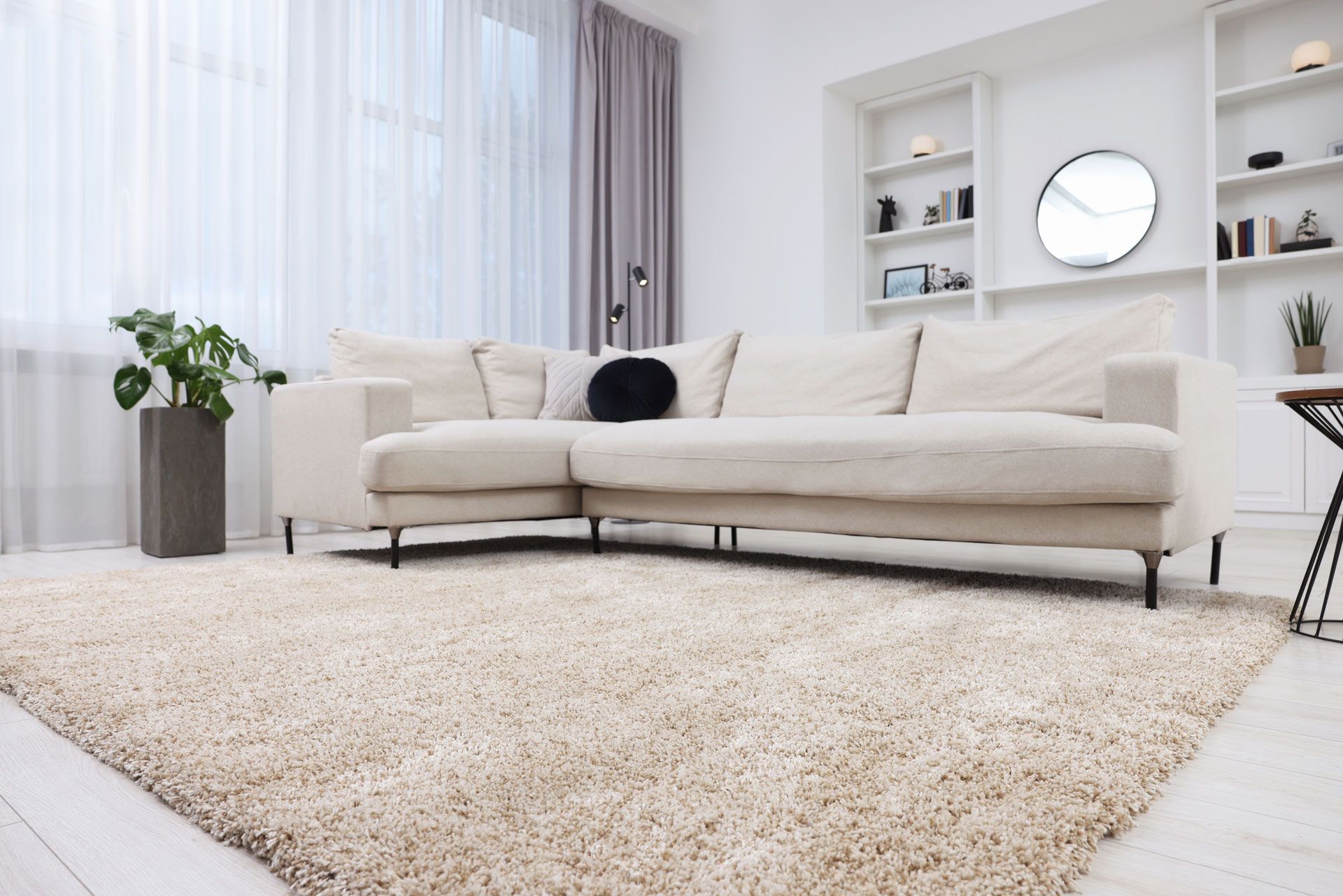 Cream-colored living room with beige sectional sofa, shaggy rug, built-in shelves, and sheer curtains.