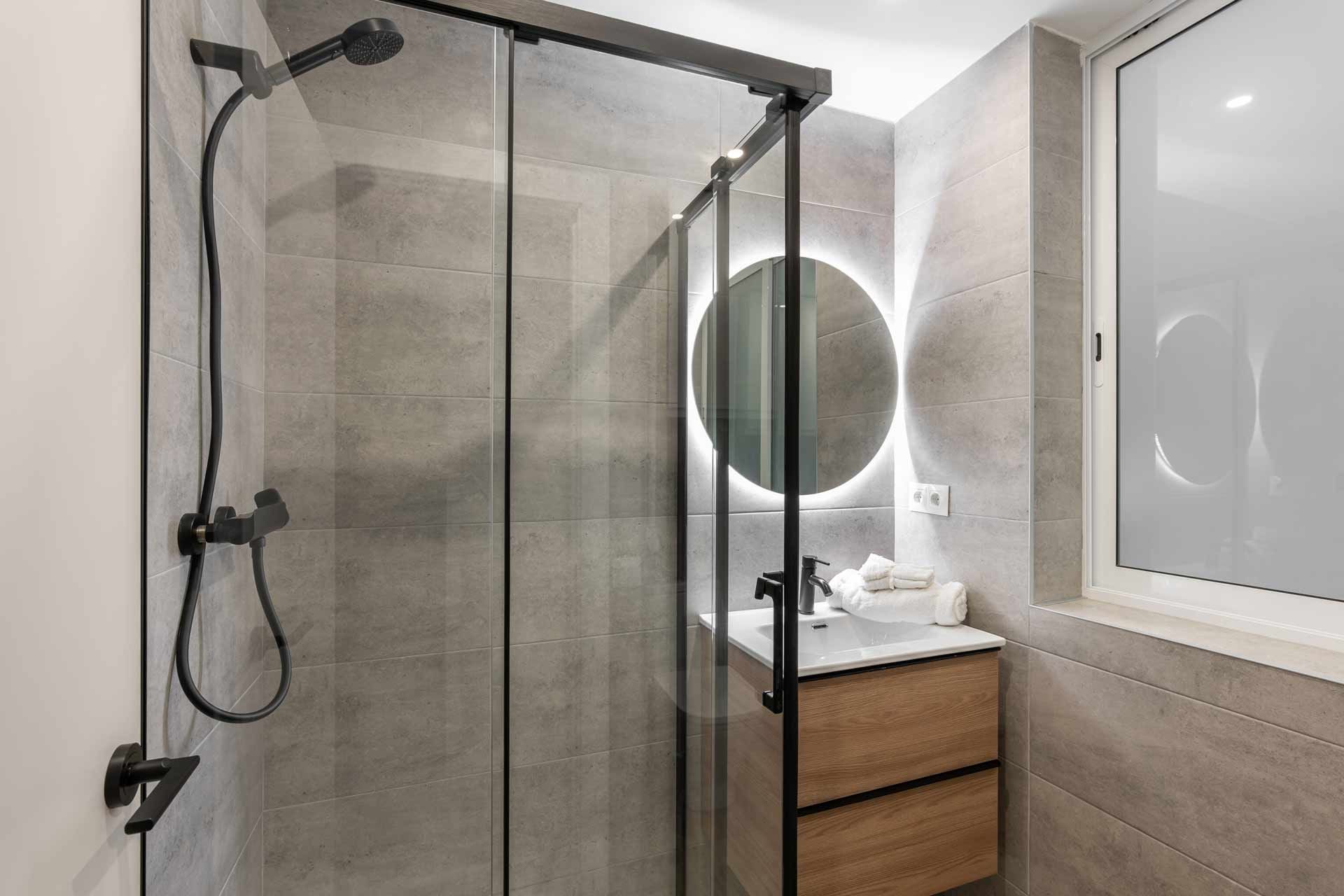 Modern bathroom with a glass shower, vanity, and round illuminated mirror.
