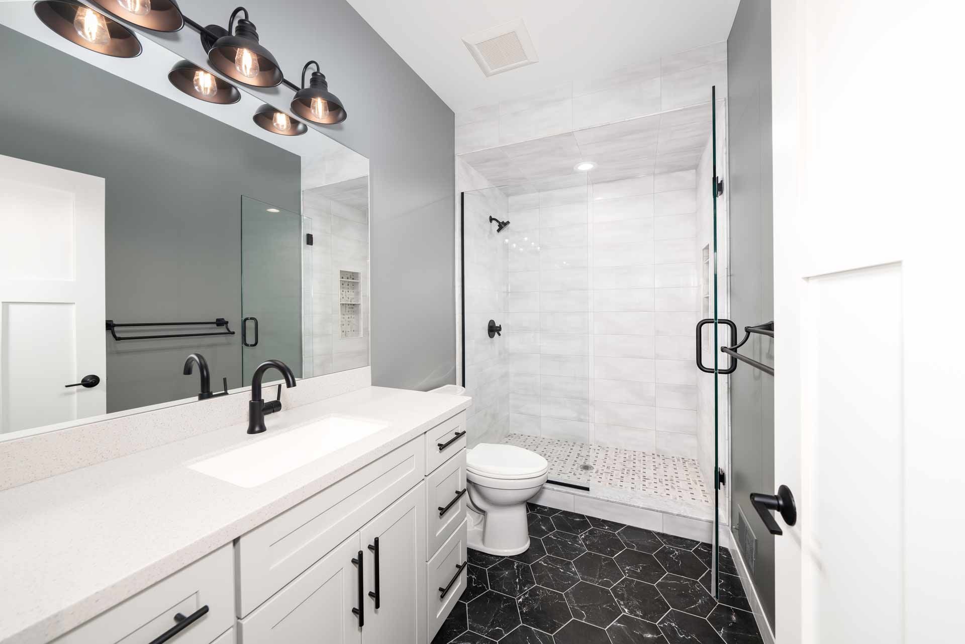Modern bathroom with white cabinets, gray walls, and black hexagonal floor tiles.