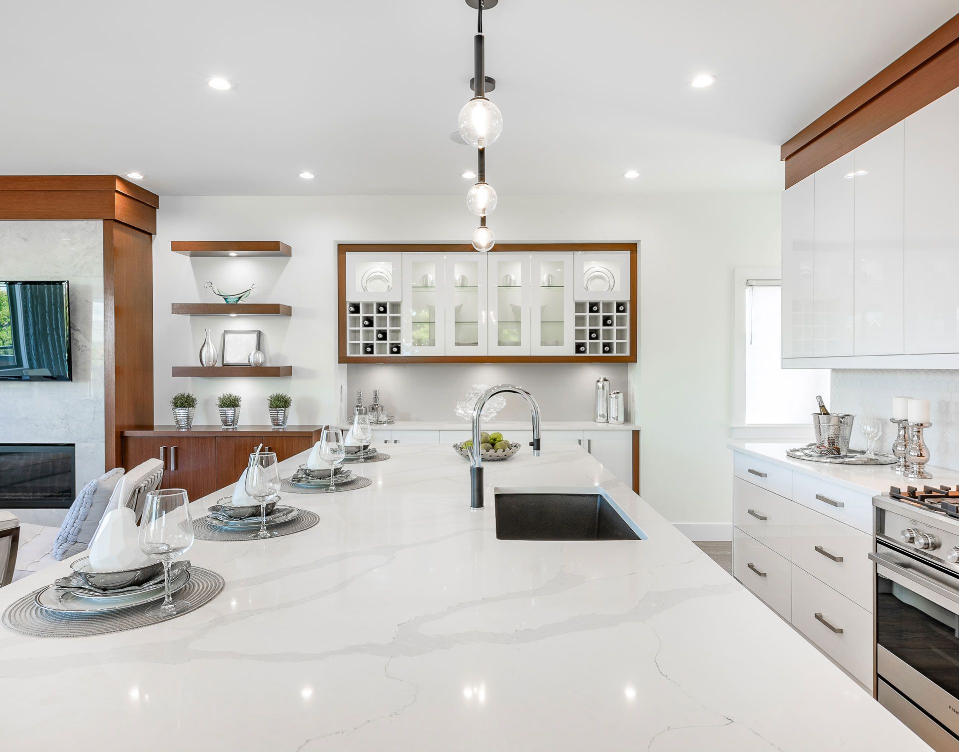 Modern white kitchen with island, marble countertops, stainless steel appliances, and wood accents.