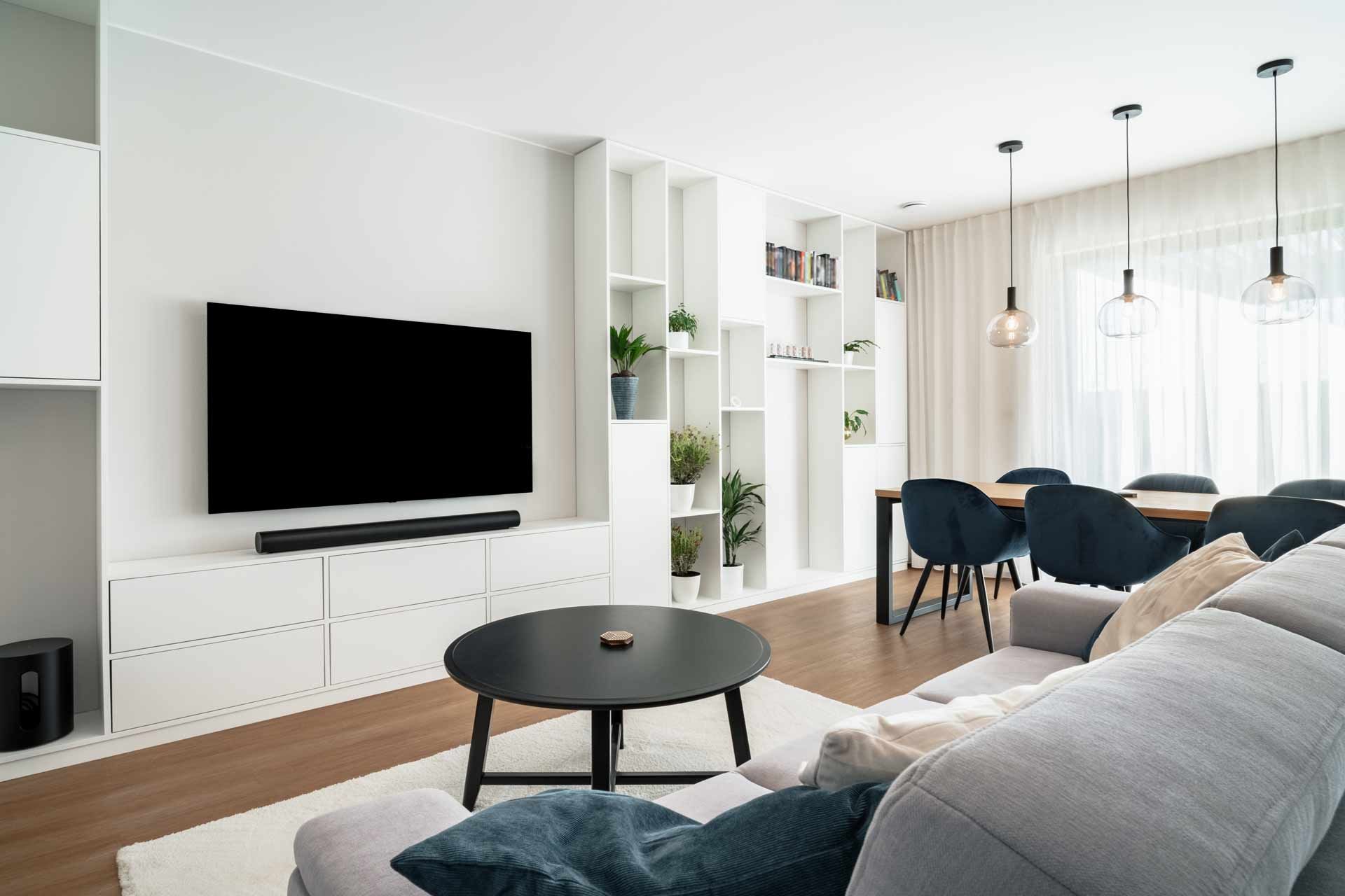 Modern living room with TV, sofa, dining area, and white shelves.