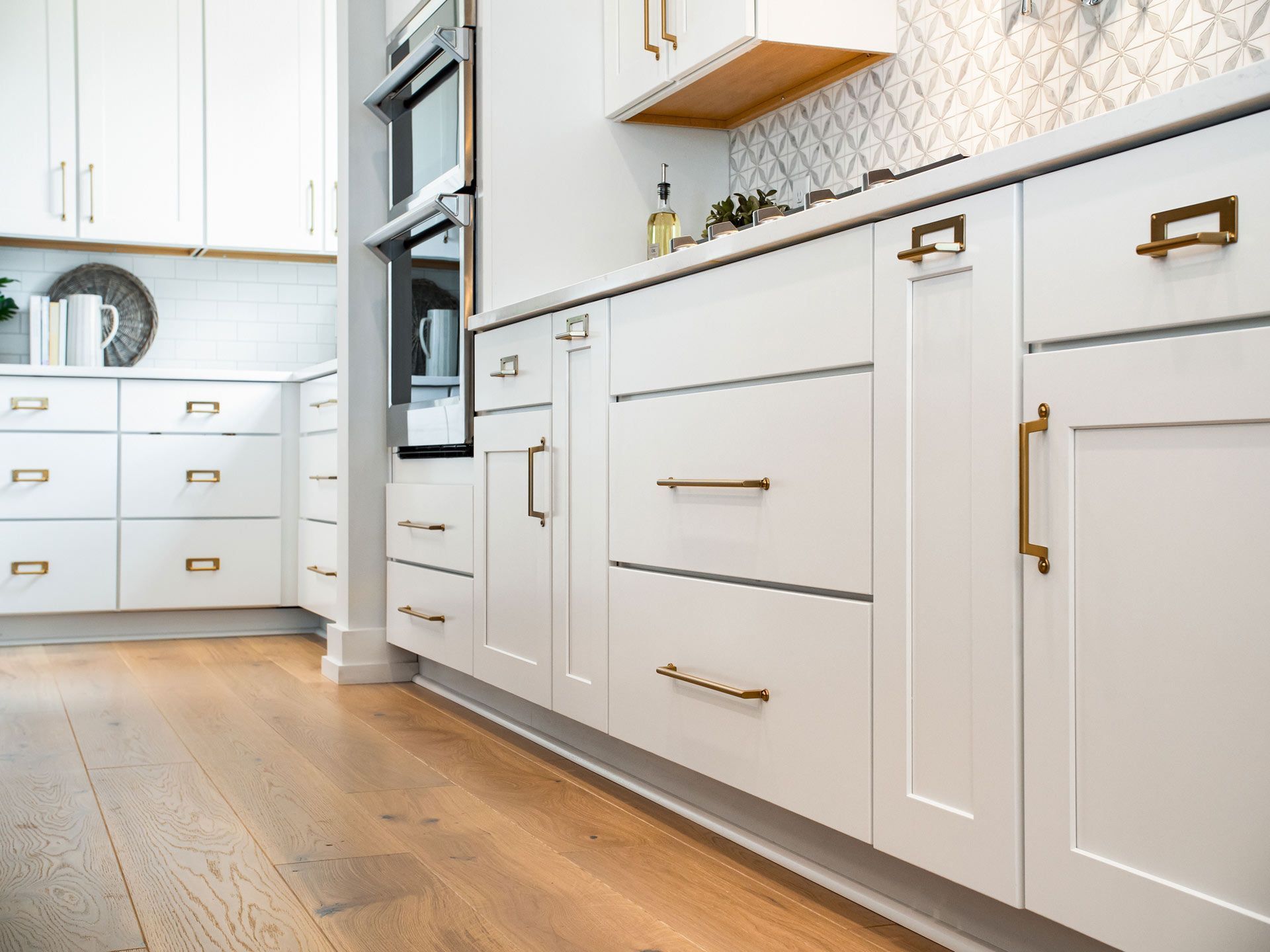 White kitchen cabinets with brass handles and light wood flooring.
