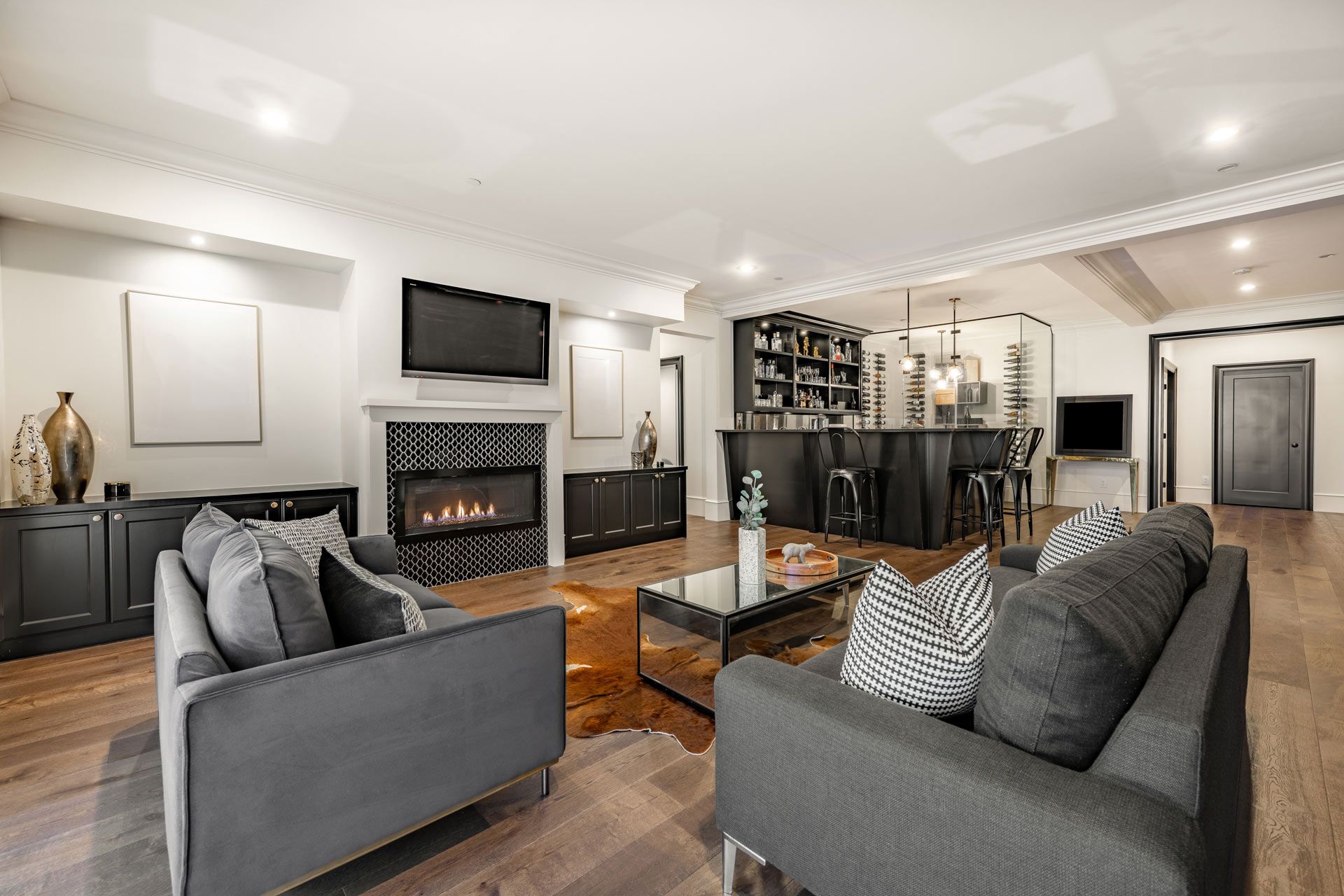 Modern living room with fireplace, bar, and two gray sofas on a hardwood floor.