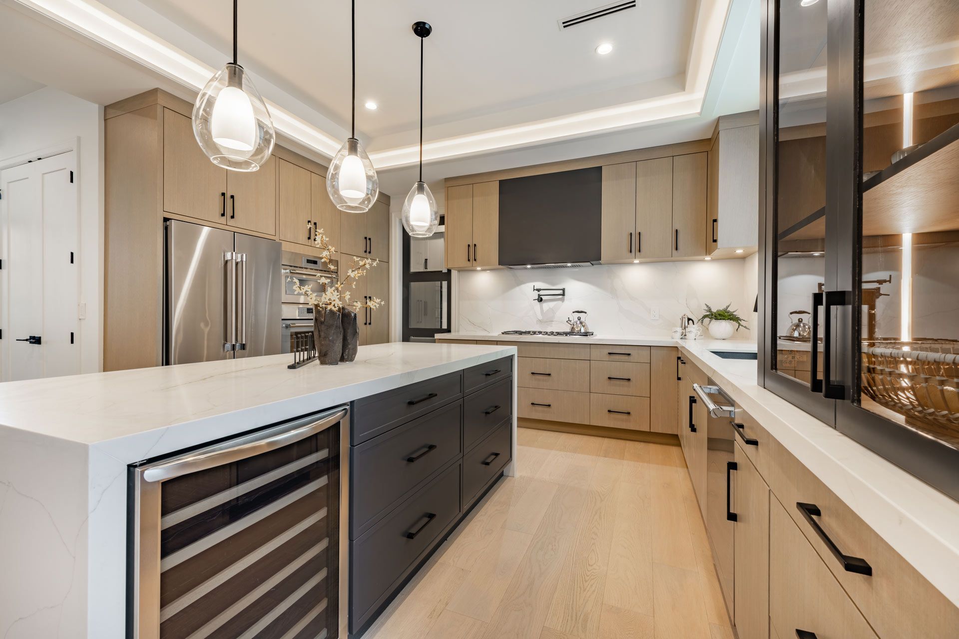 Modern kitchen with gray island, light wood cabinets, stainless steel appliances, and pendant lights.