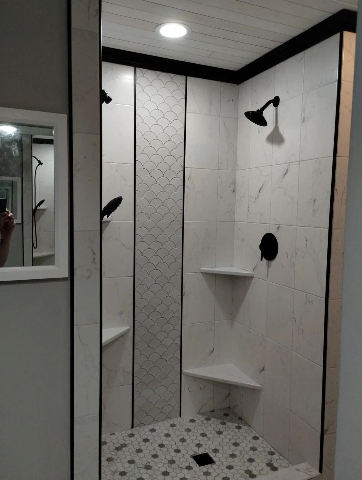 Modern shower with white marble-look tiles, black fixtures, patterned accent, and recessed shelves.
