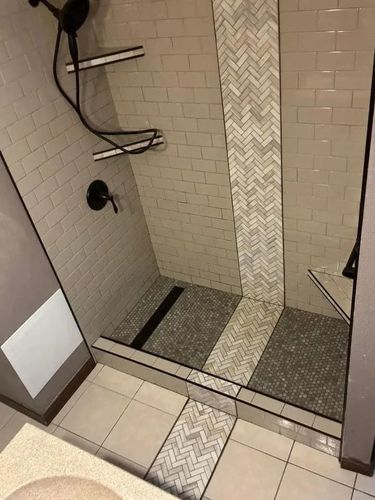 Shower with gray and white tile, pebble floor, and shelves.