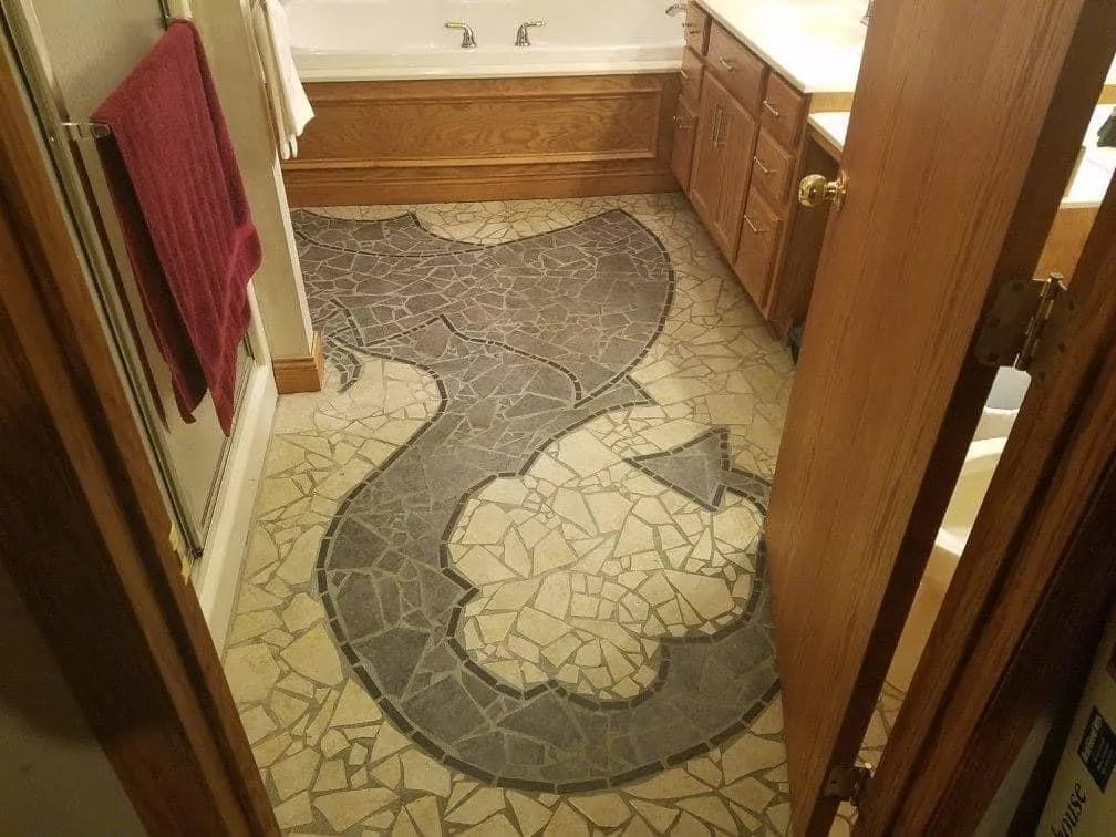 Bathroom with mosaic floor art in shades of gray and white, wooden cabinets and trim.