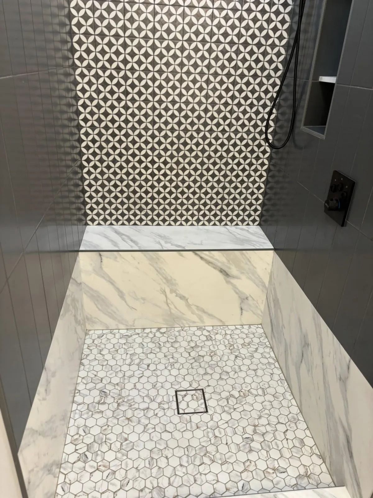 Modern shower with patterned tile, marble accents, and a mosaic floor.