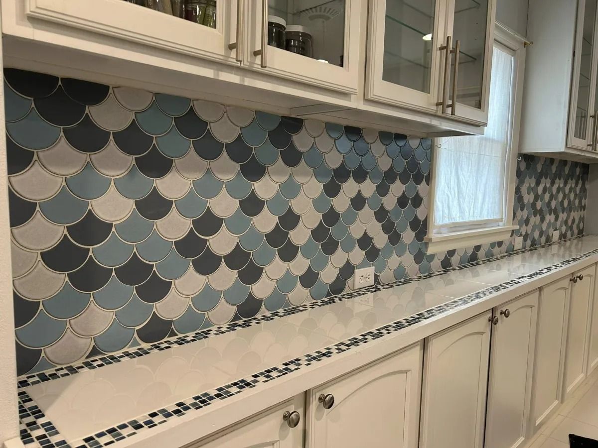 Kitchen with white cabinets, blue, gray, and white scale-patterned backsplash, and white countertops.