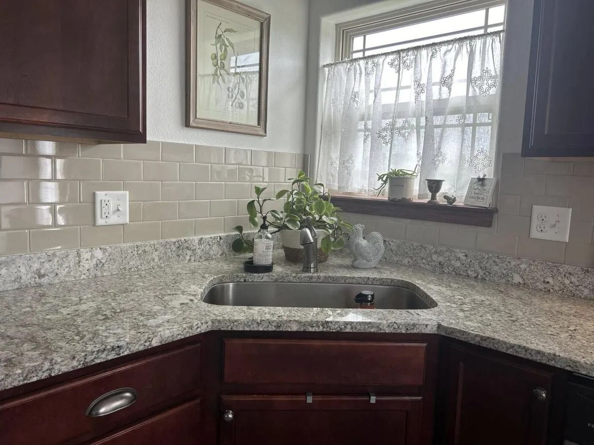 Kitchen corner with granite countertop, sink, and window with sheer curtain.