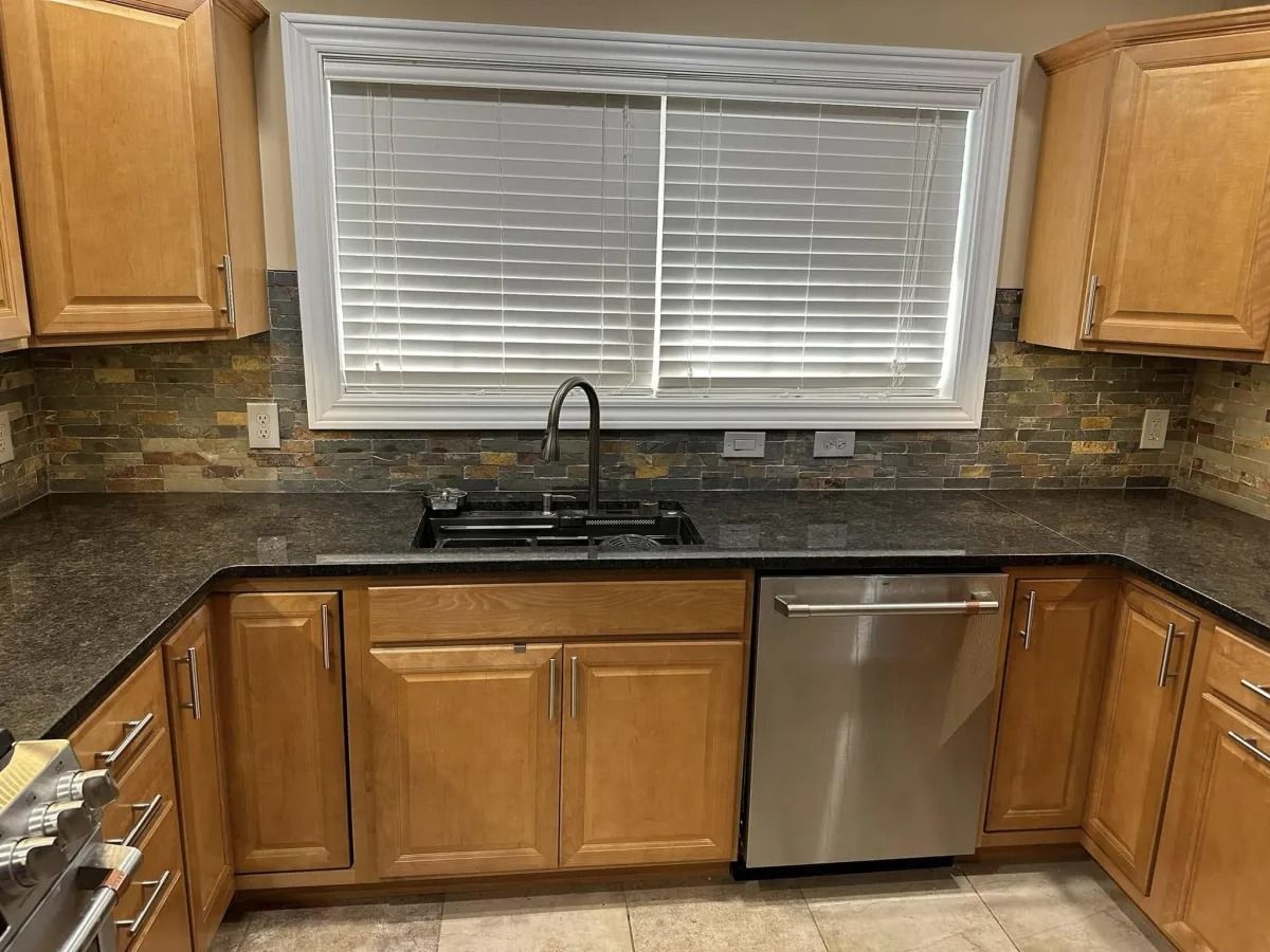 Kitchen with light wood cabinets, granite countertops, stainless steel appliances, and a window with blinds.