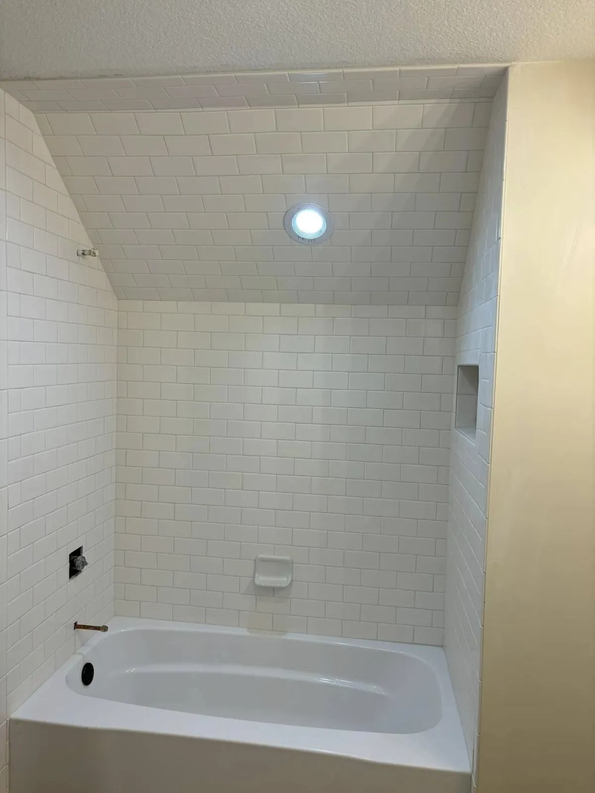 White tiled bathroom with a tub, recessed light, and a niche.