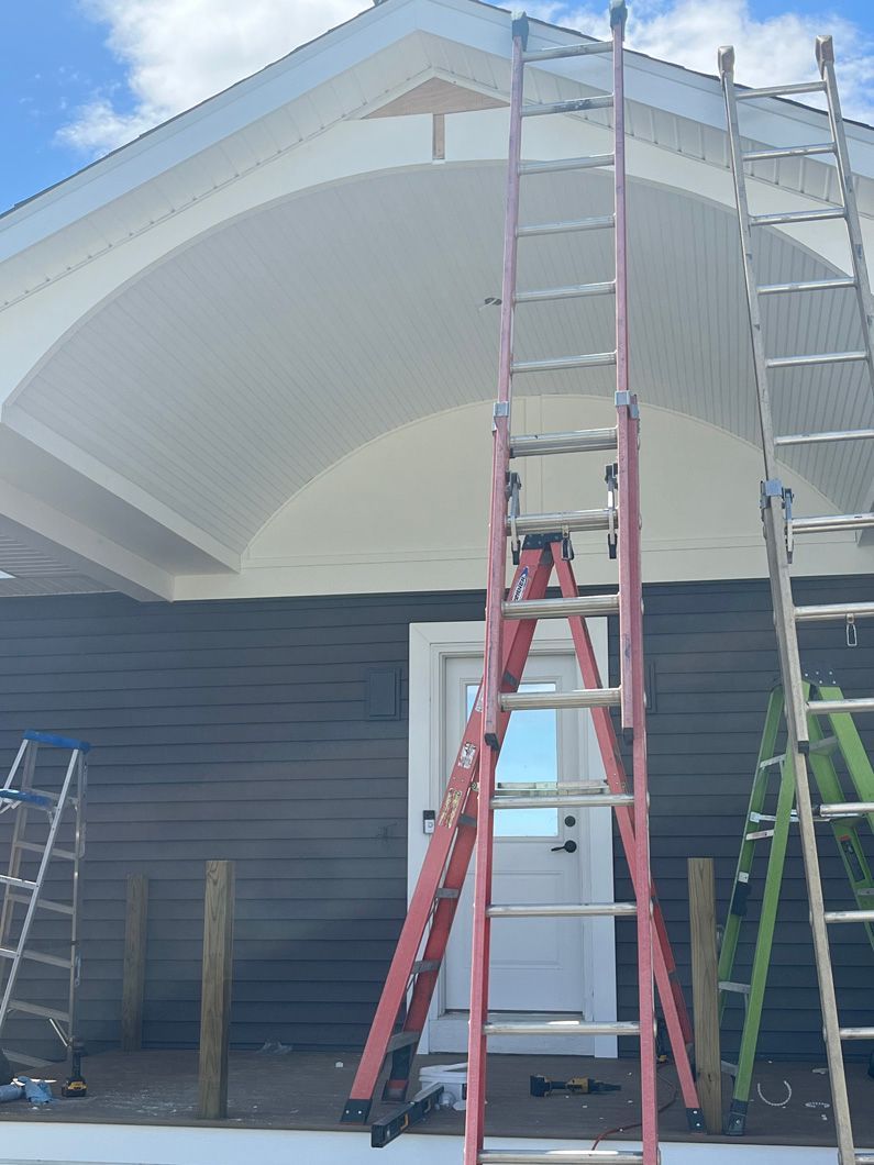 Red and silver ladders leaning against a white building with dark blue siding, under a blue sky.