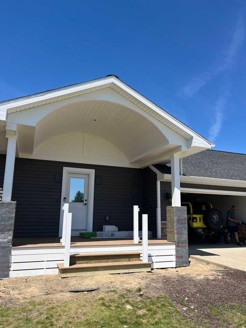 Dark gray house with white trim, porch, and a partial carport; blue sky.