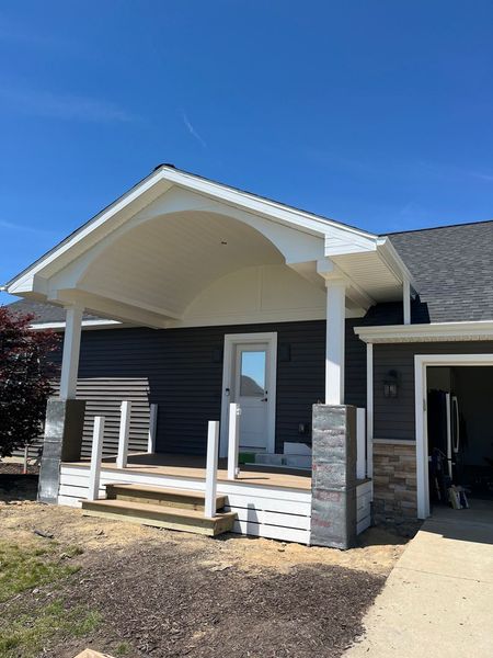 Dark blue house with white porch roof and pillars, white door, and light gray siding.