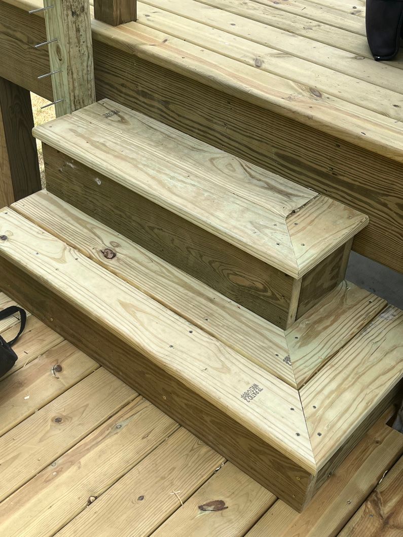 Wooden deck stairs. Two steps with a dark-stained wood border. Outdoors, daylight.