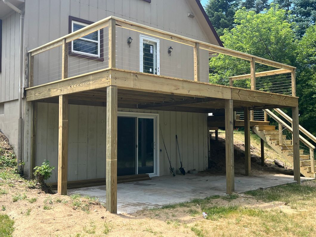 Two-level wooden deck attached to a house. The top level has railings. Stairs lead down.