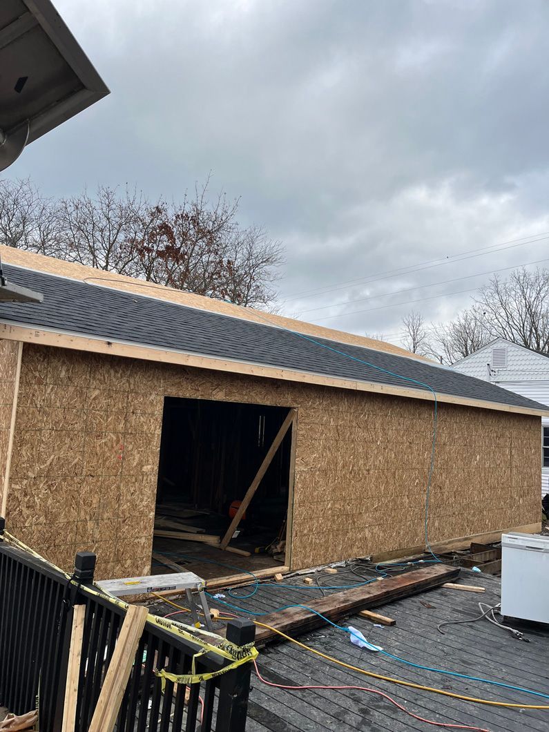 Garage under construction with OSB walls, dark roof, and open doorway; overcast sky.