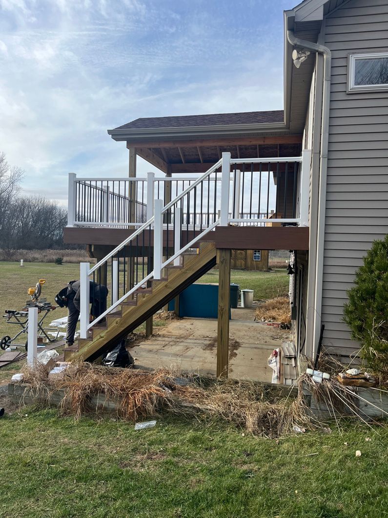 A deck with stairs attached to a house. A person works on the deck.