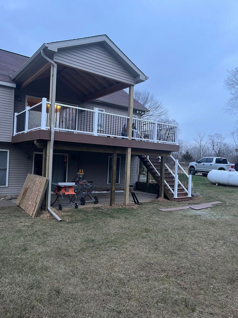 Two-story home with wooden deck. Person working below deck; white railing and brown deck.